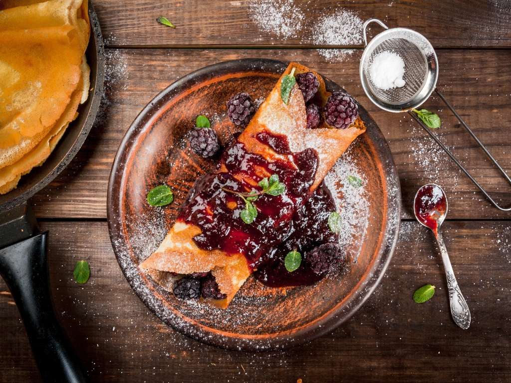 Блин с ягодами и джемом на тарелке с сахарной пудрой