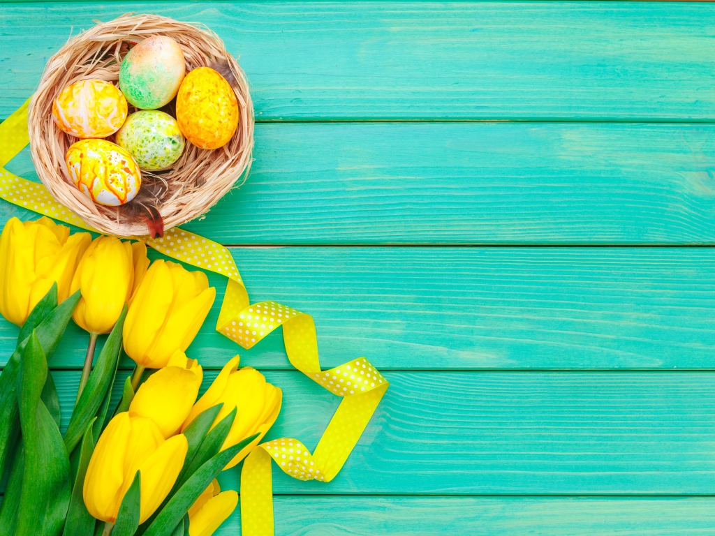 Разноцветные пасхальные яйца  и букет желтых тюльпанов на голубом фоне