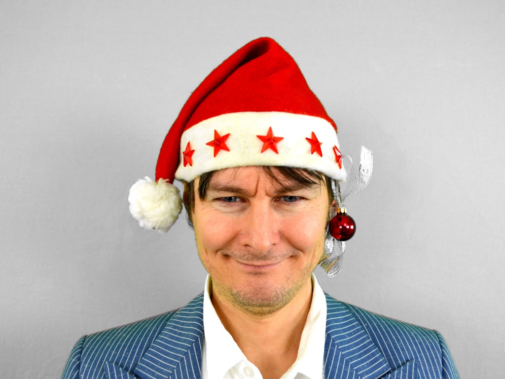 Голубоглазый мужчина в новогодней шапке на сером фоне 