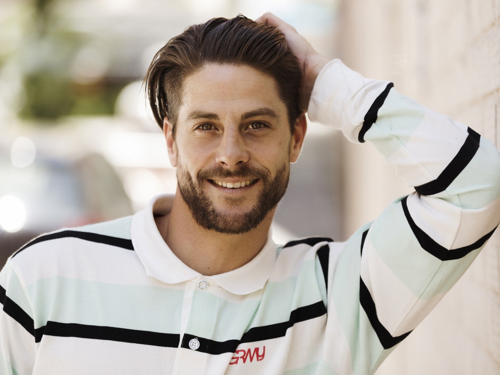 Улыбающийся мужчина в рубашке стоит у стены