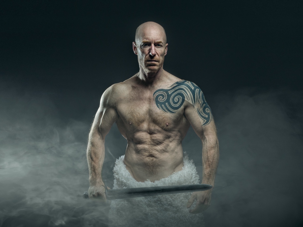 Сильный мужчина с мечом с татуировками на теле 