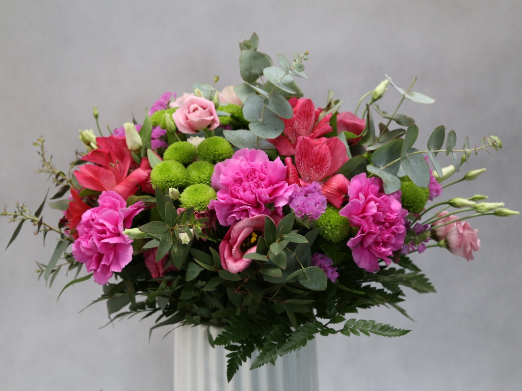 Красивый разноцветный букет в белой вазе на фоне серой стены 