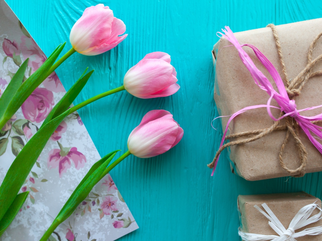 Три розовых тюльпана на голубом столе с подарками