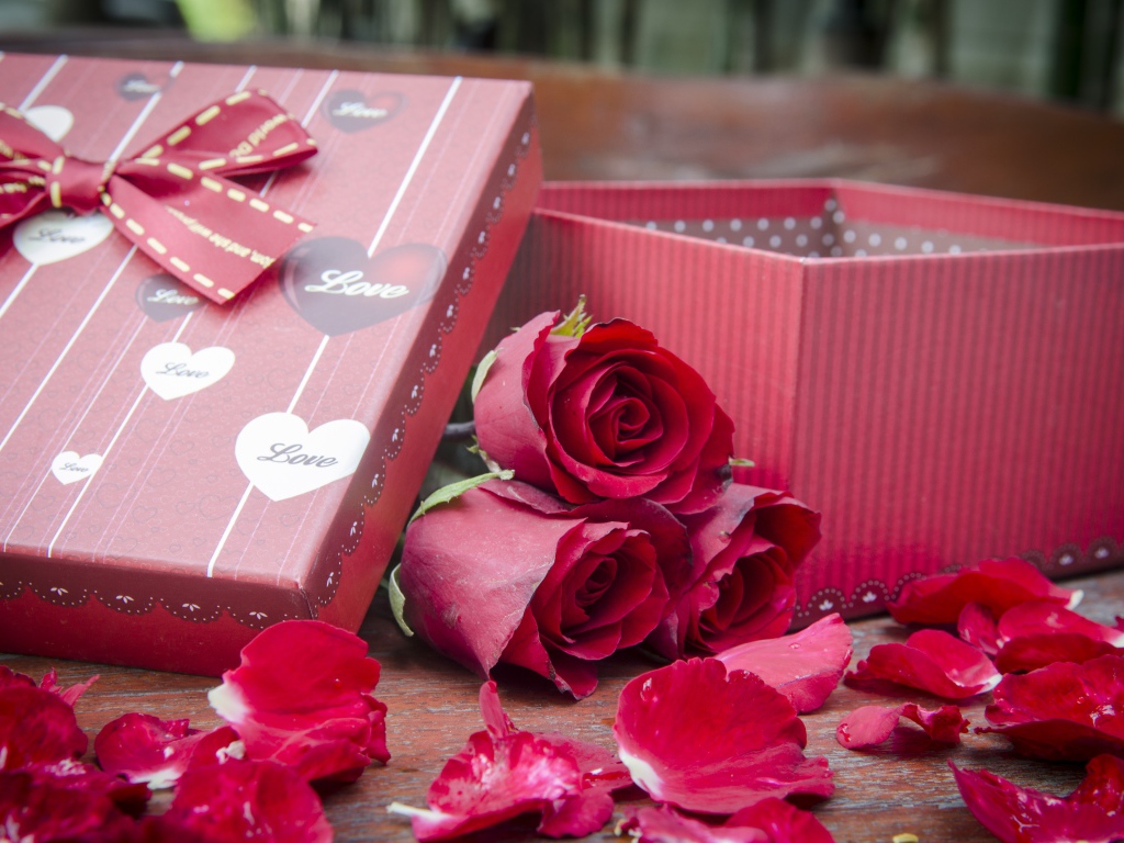 Три красные розы с лепестками  на столе с подарком