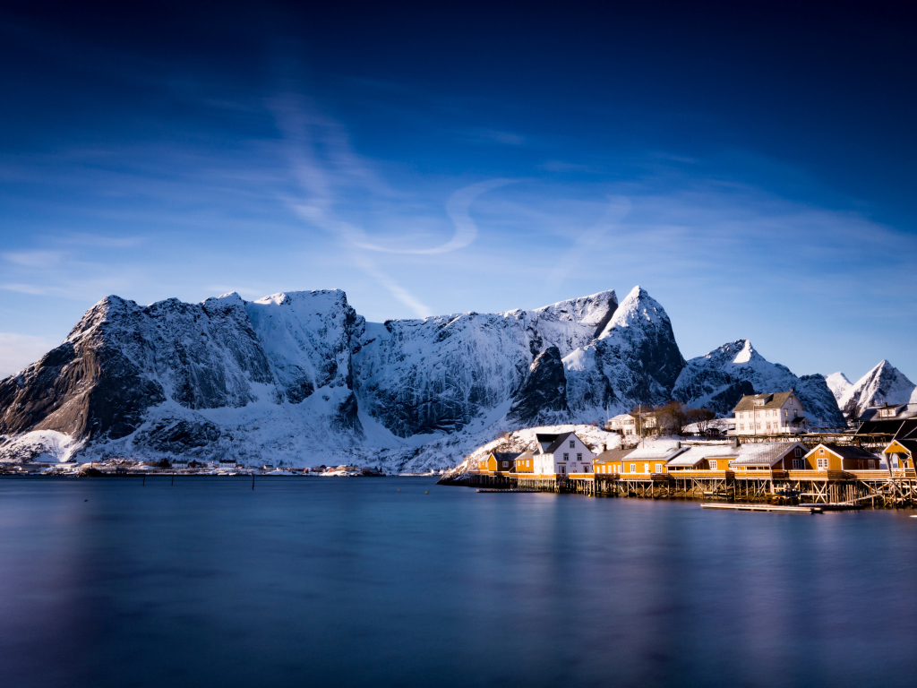 Красивый вид на дома у заснеженных гор под голубым небом 
