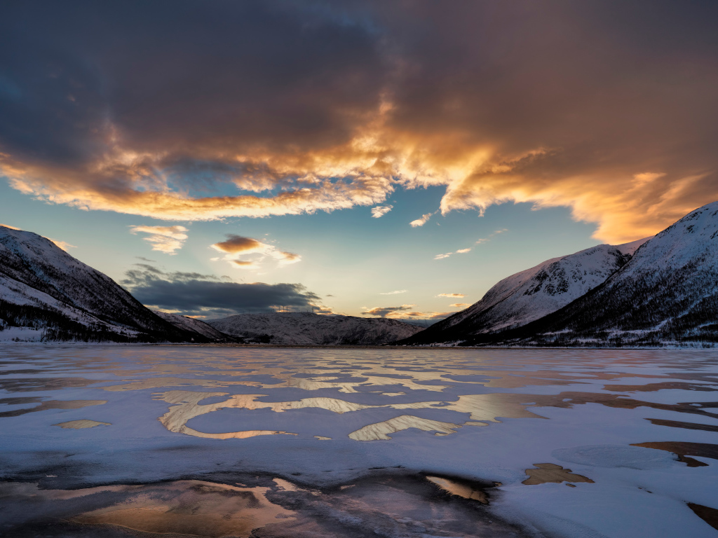 Покрытое льдом озеро у гор на закате солнца 