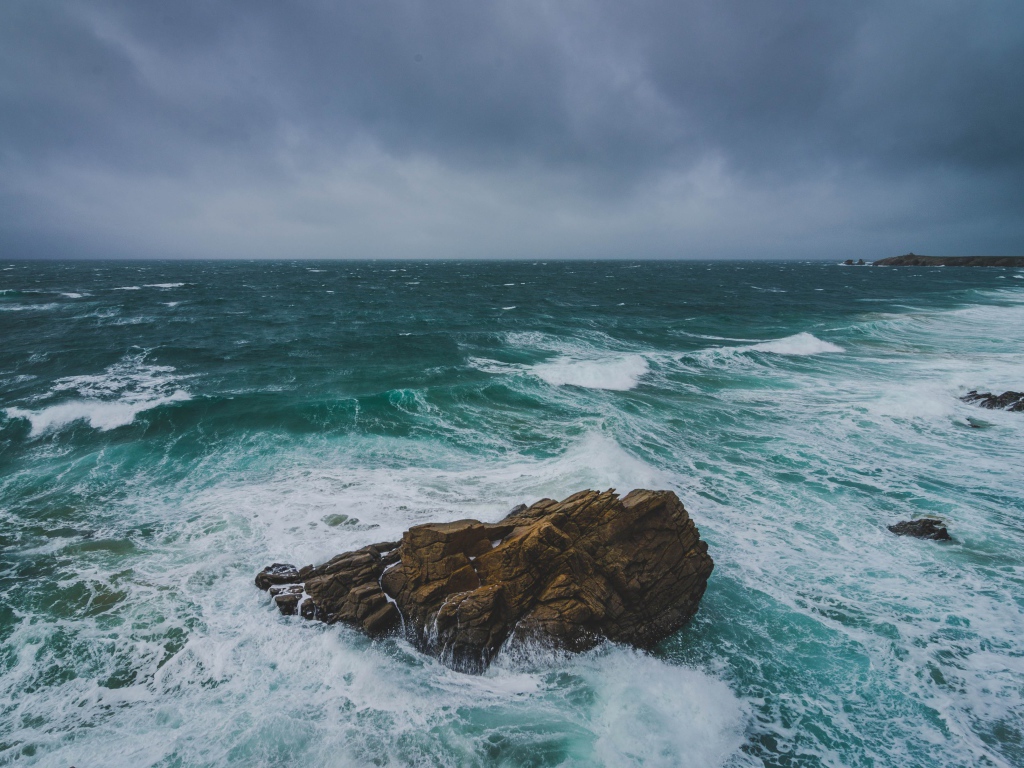 Большой камень омывают белые волны океана 