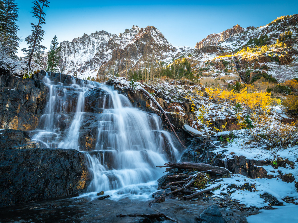 Красивый водопад стекает по холодным камням на фоне заснеженных гор