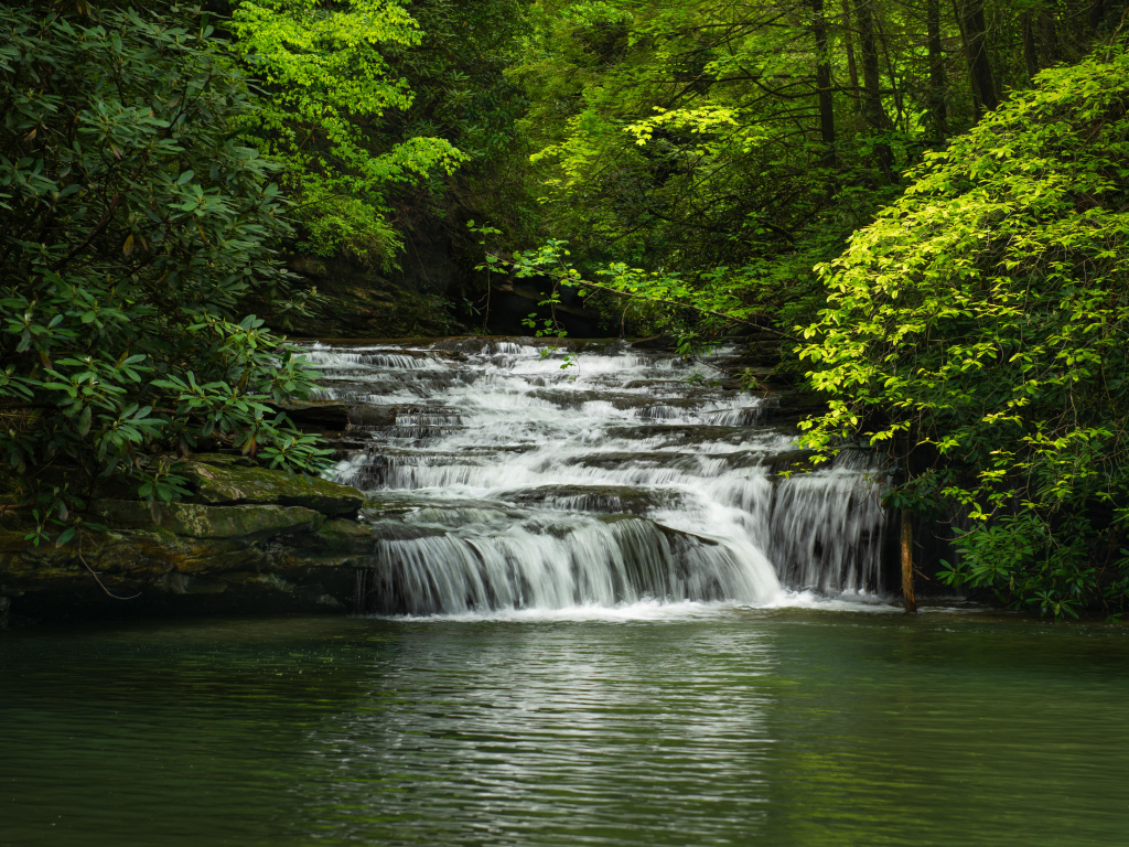 Водопад стекает по каменному каскаду в реку 