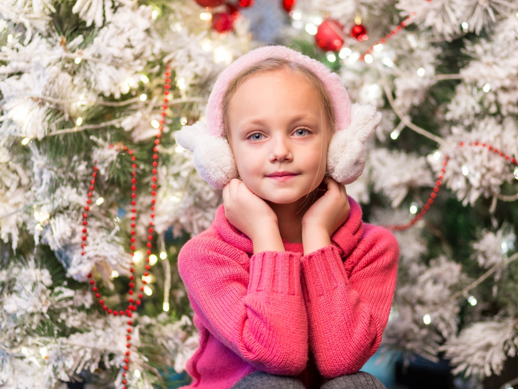 Девочка в розовых наушниках сидит у ели