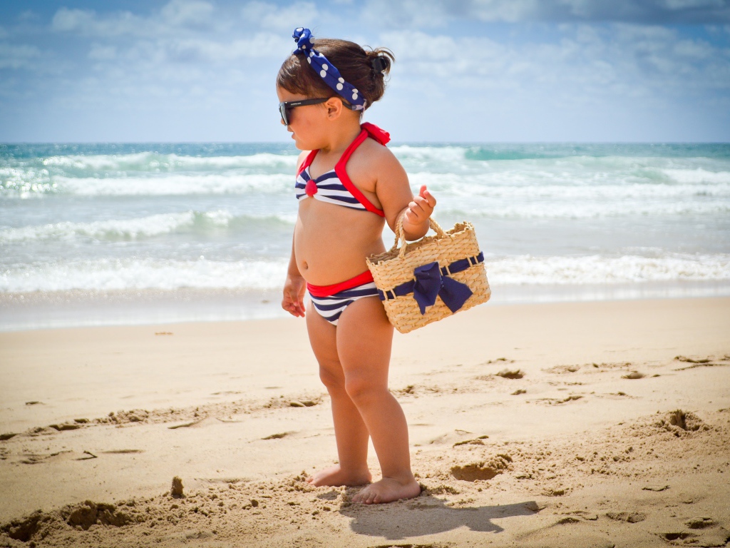 Маленькая девочка в купальнике гуляет по пляжу 