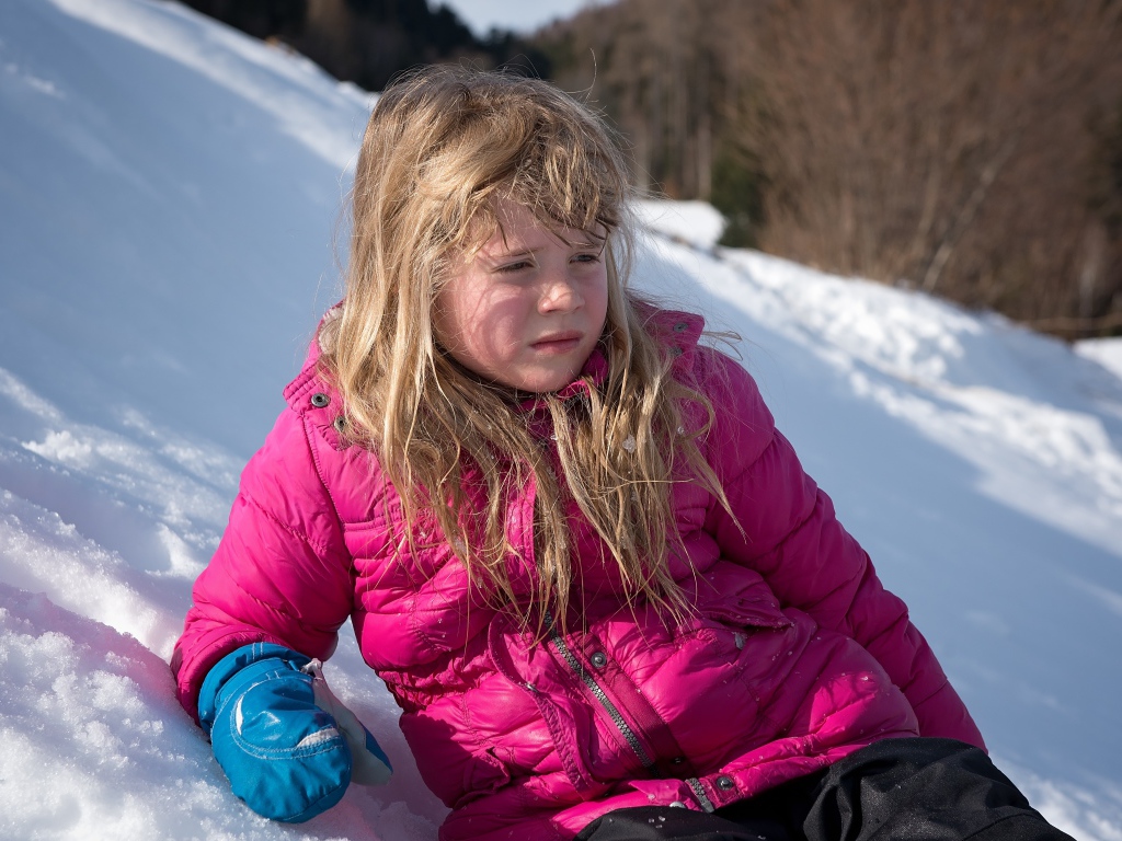 Маленькая девочка лежит на заснеженной горке 