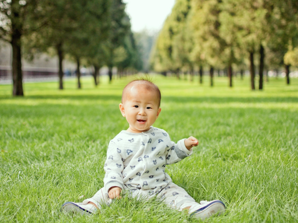 Маленький ребенок азиат сидит на зеленой траве 