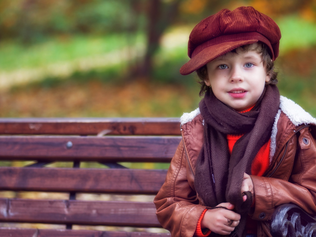 Маленький мальчик в кепке сидит на лавке