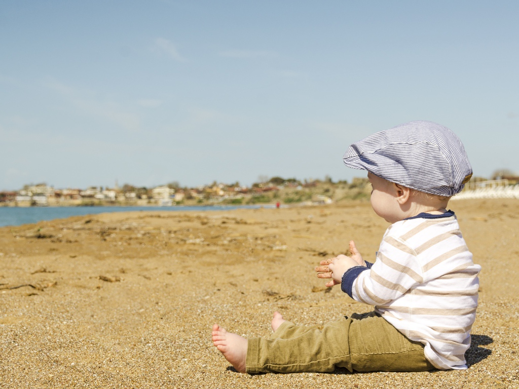 Маленький мальчик сидит на песке у реки