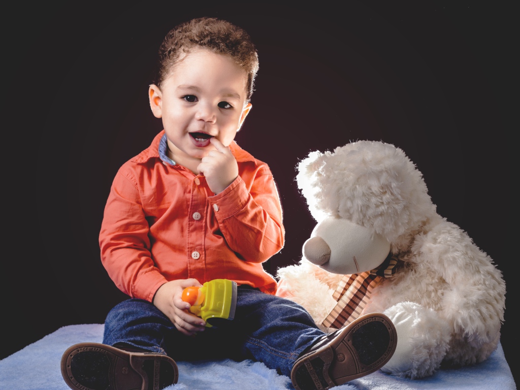 Маленький мальчик с игрушечным медведем на черном фоне