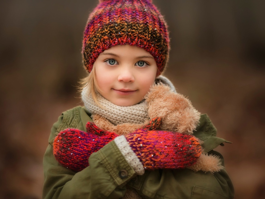Маленькая девочка в теплой шапке и варежках  с игрушкой в руках 