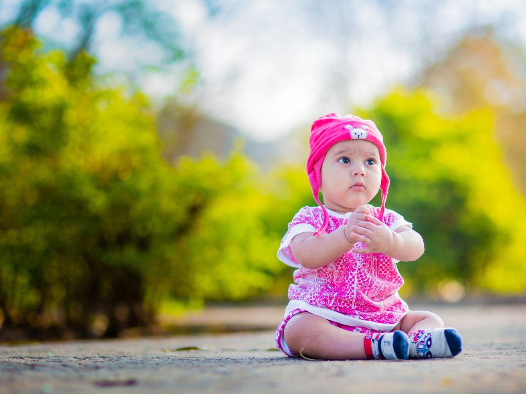 Маленькая девочка в розовом костюме сидит на земле