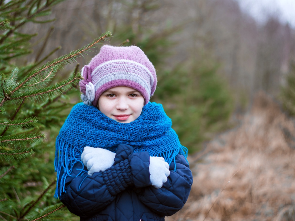 Маленькая девочка в теплой одежде у ели