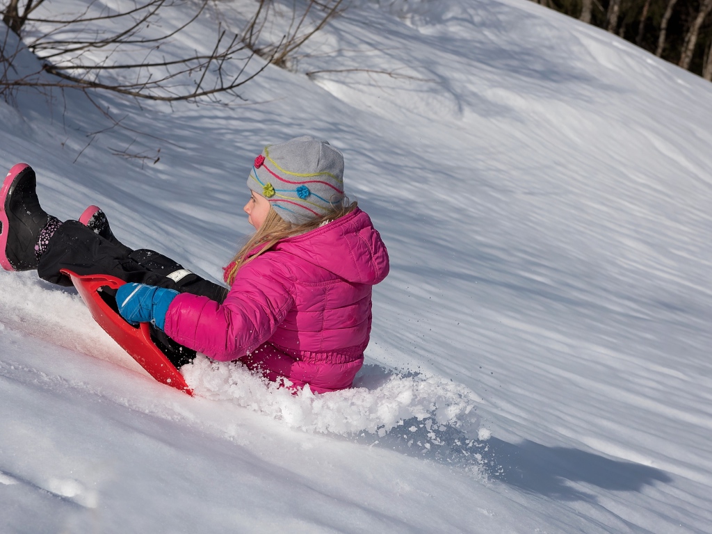 Маленькая девочка катится с заснеженной горки 