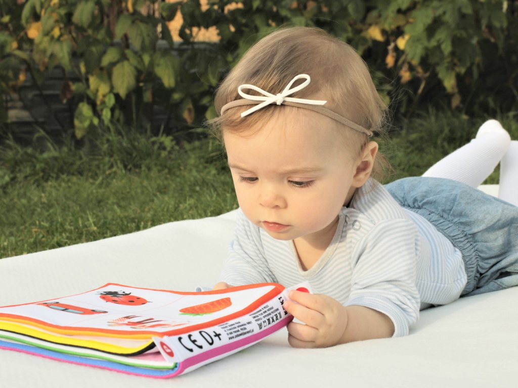 Маленькая девочка лежит на покрывале с книгой