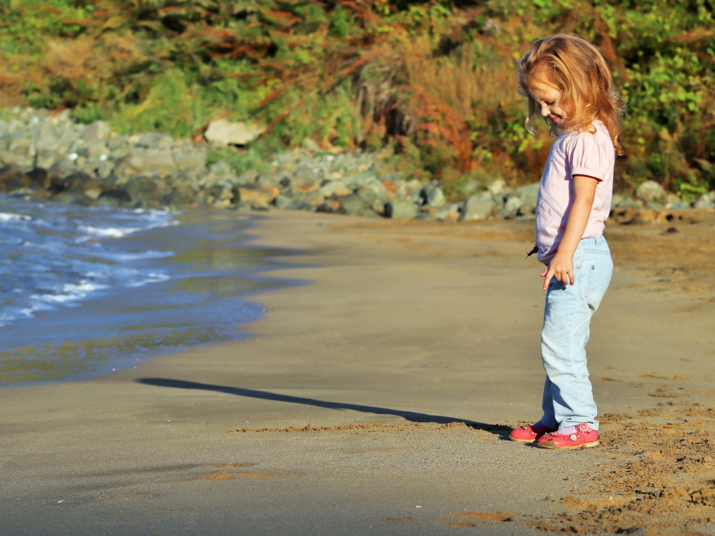 Маленькая девочка гуляет по мокрому песку 