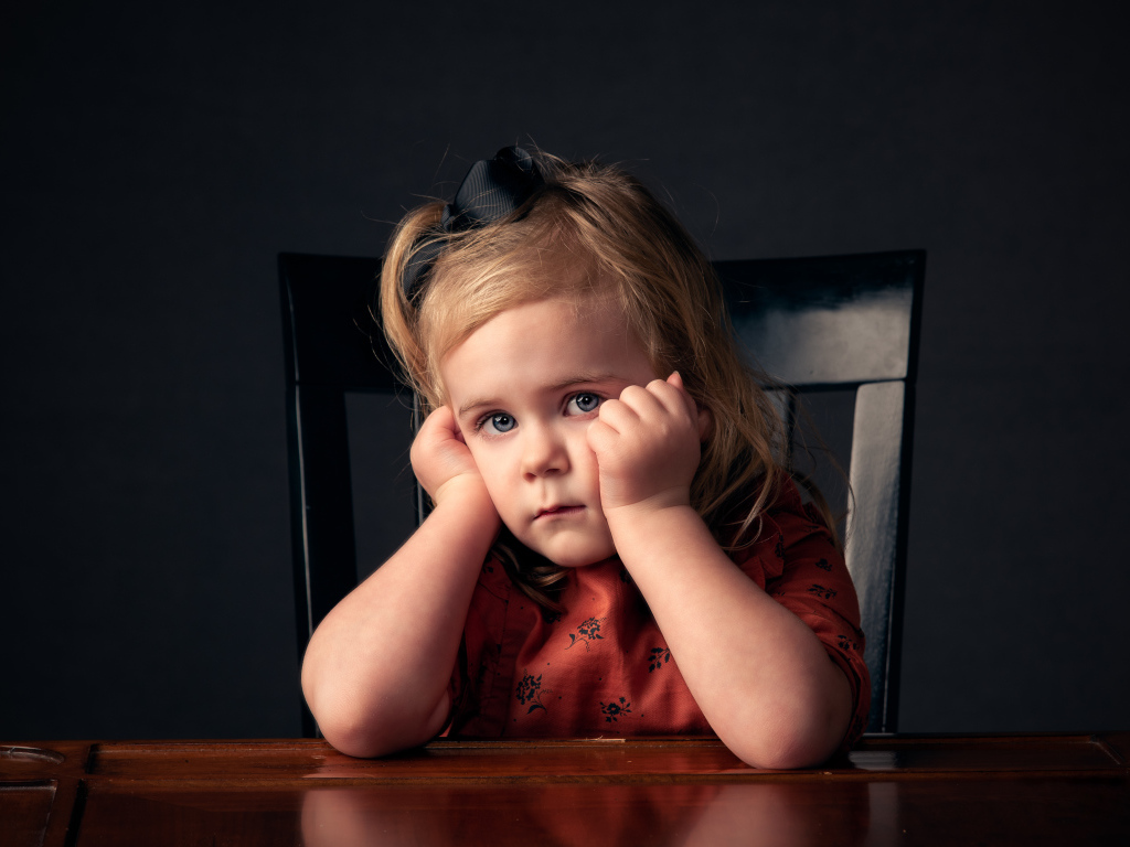 Грустная маленькая девочка сидит на черном стуле