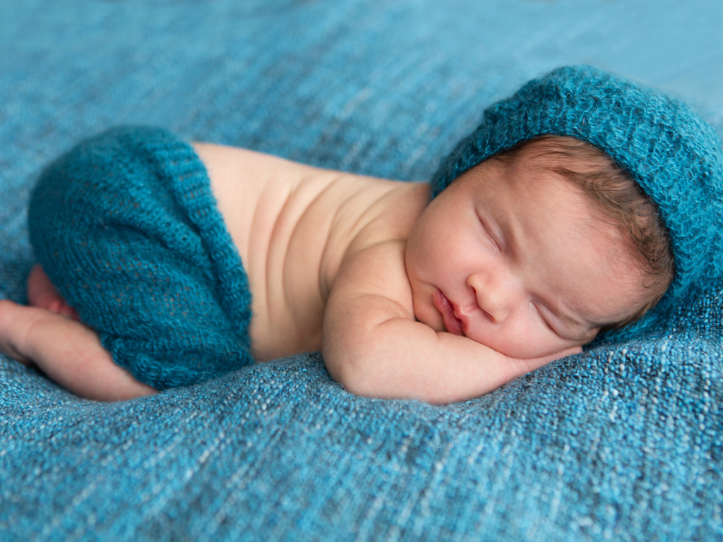 Спящий грудной ребенок лежит на голубом покрывале 