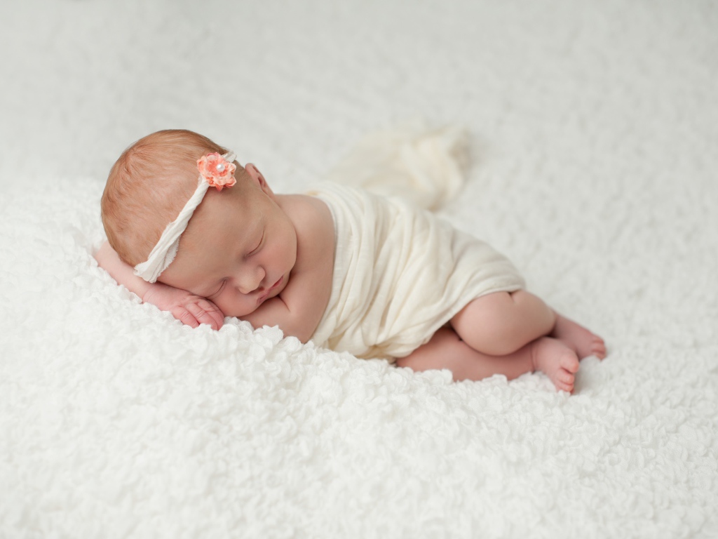 Маленький грудной ребенок спит на белом покрывале 