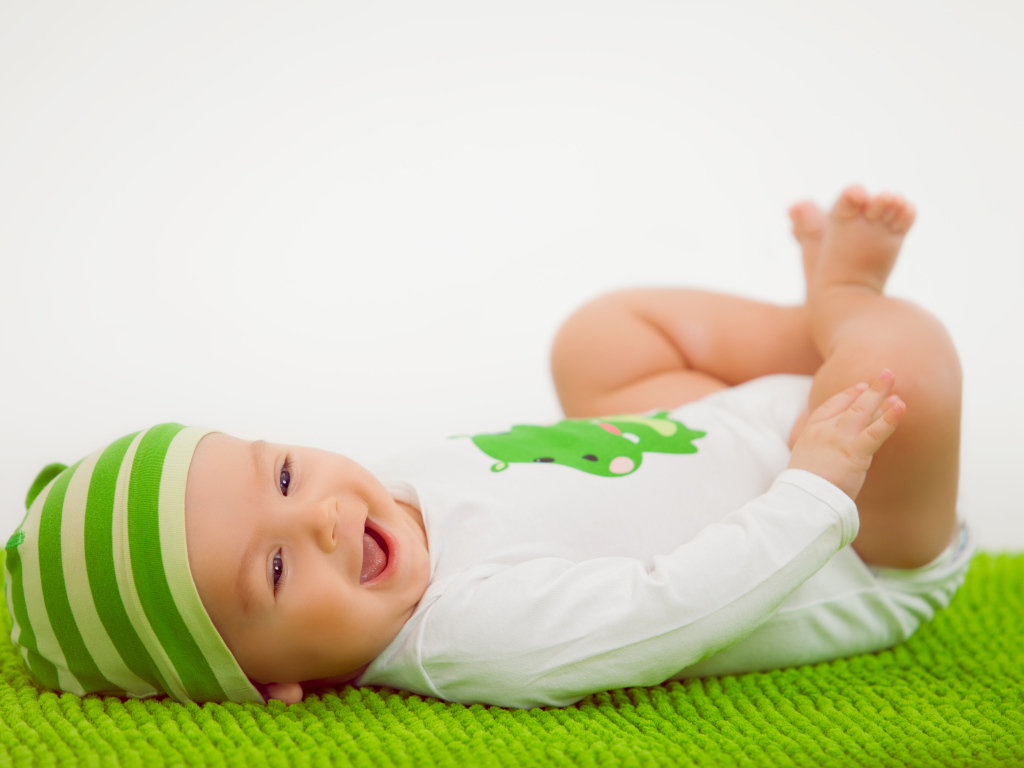 Улыбающийся маленький ребенок лежит на зеленом покрывале 