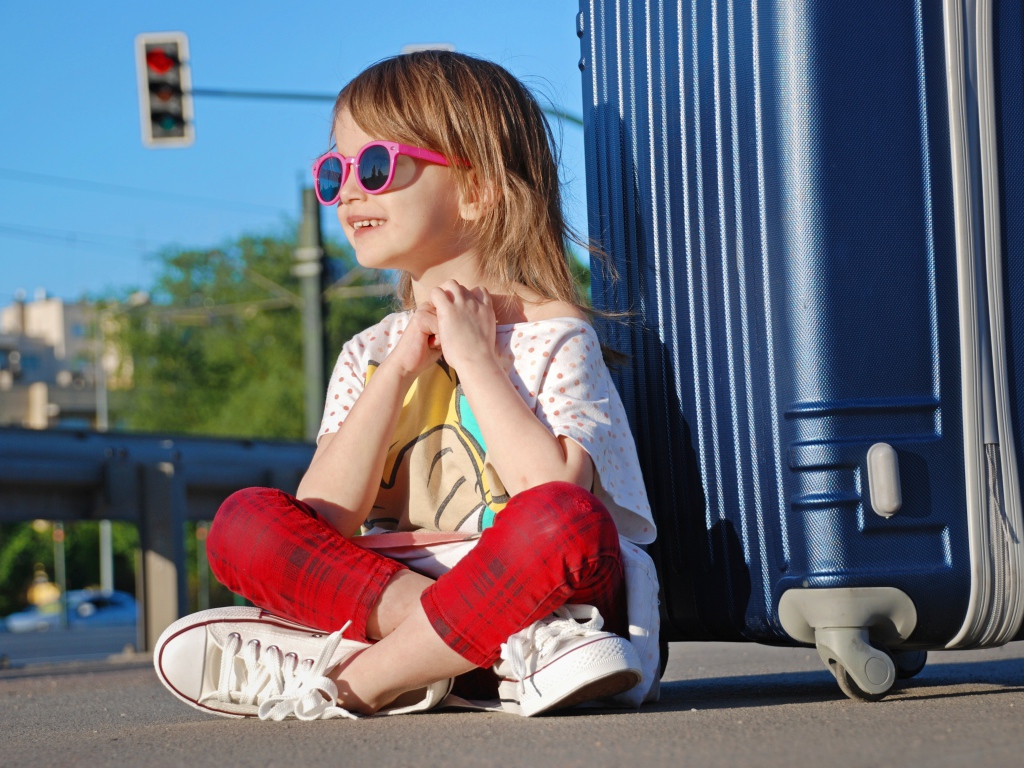 Улыбающаяся маленькая девочка в очках с чемоданом