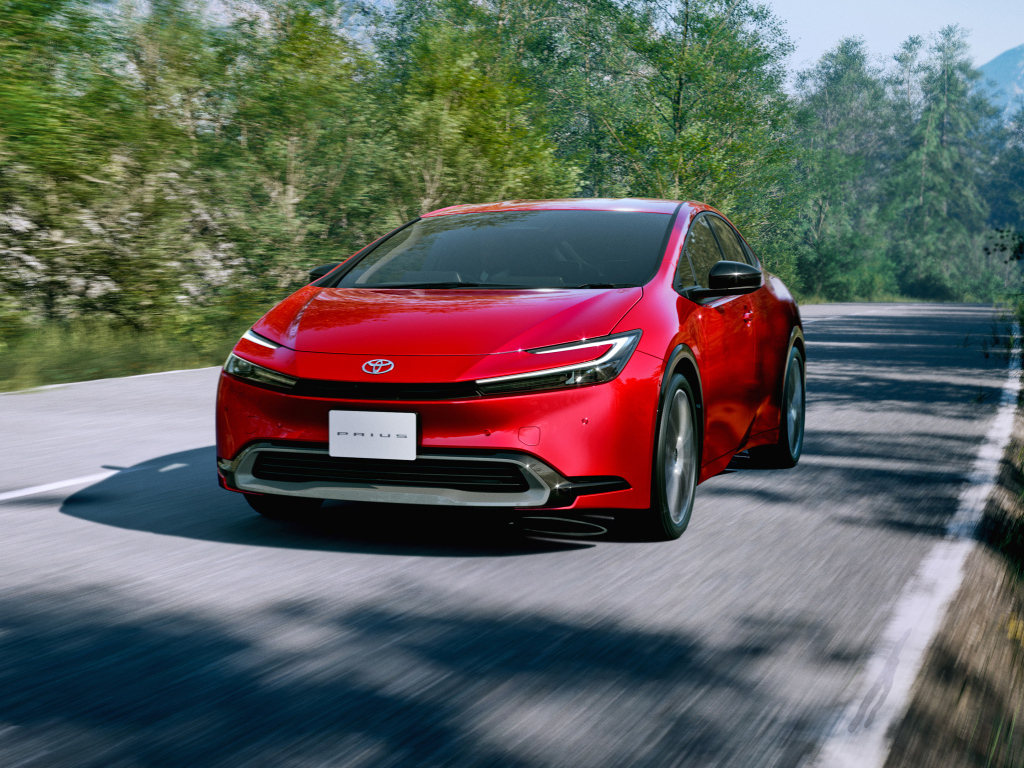 Красный автомобиль Toyota Prius HEV 2023  года на дороге