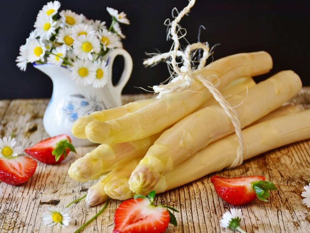 Спаржа на столе с ромашками и ягодами клубники