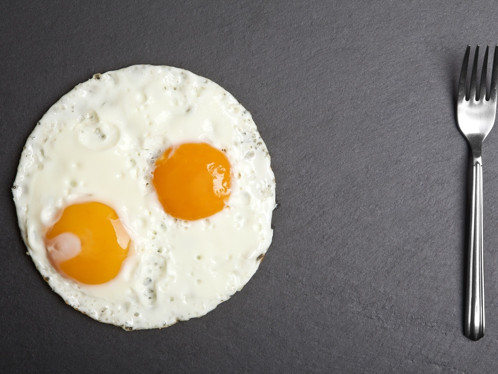 Яичница глазунья с вилкой на сером столе