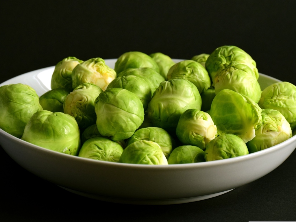 Зеленая брюссельская капуста в тарелке на черном фоне