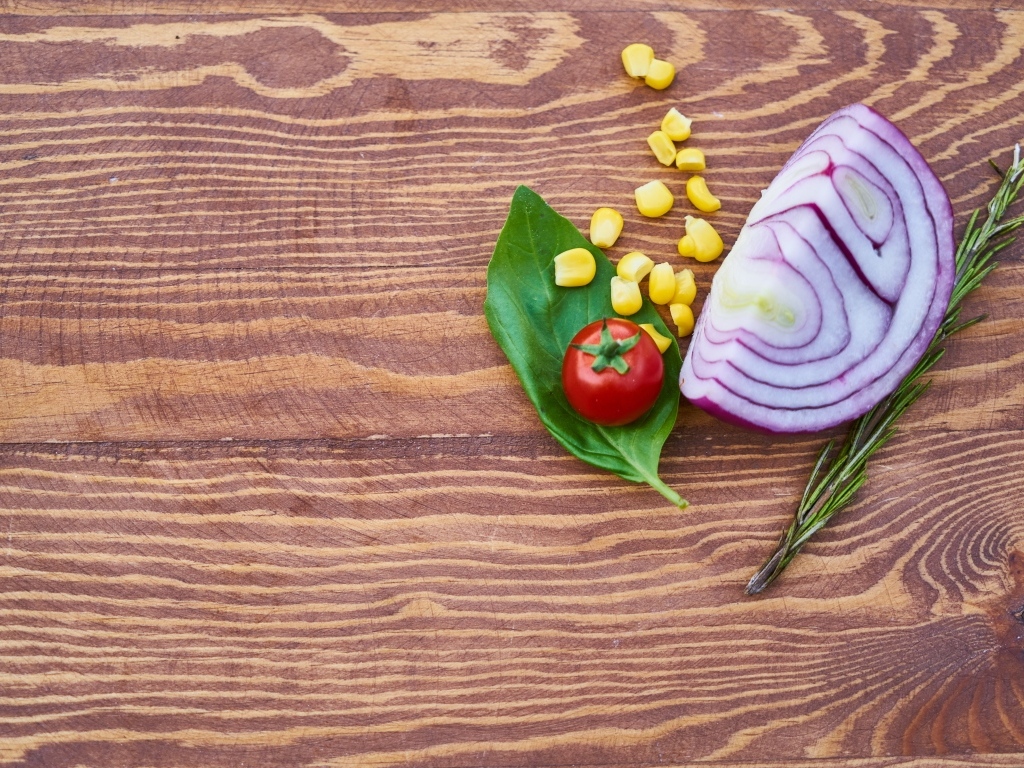 Половина лука на столе с кукурузой и помидором