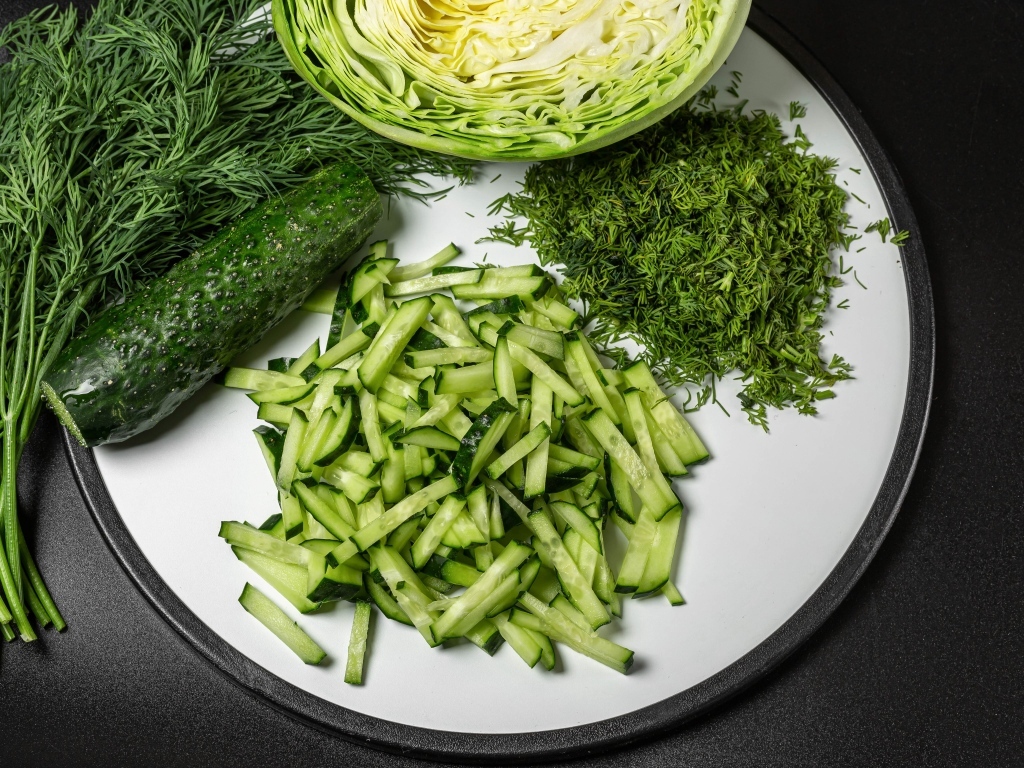 Нарезанные огурцы на столе с капустой и укропом