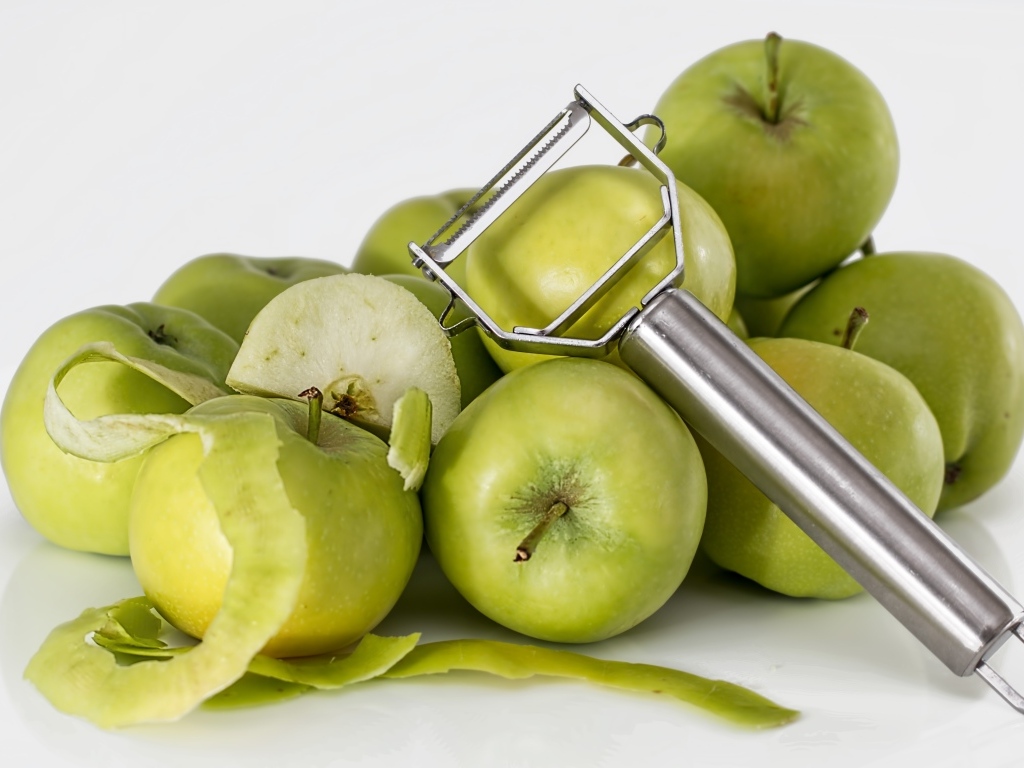 Зеленые яблоки с овощечисткой на белом фоне
