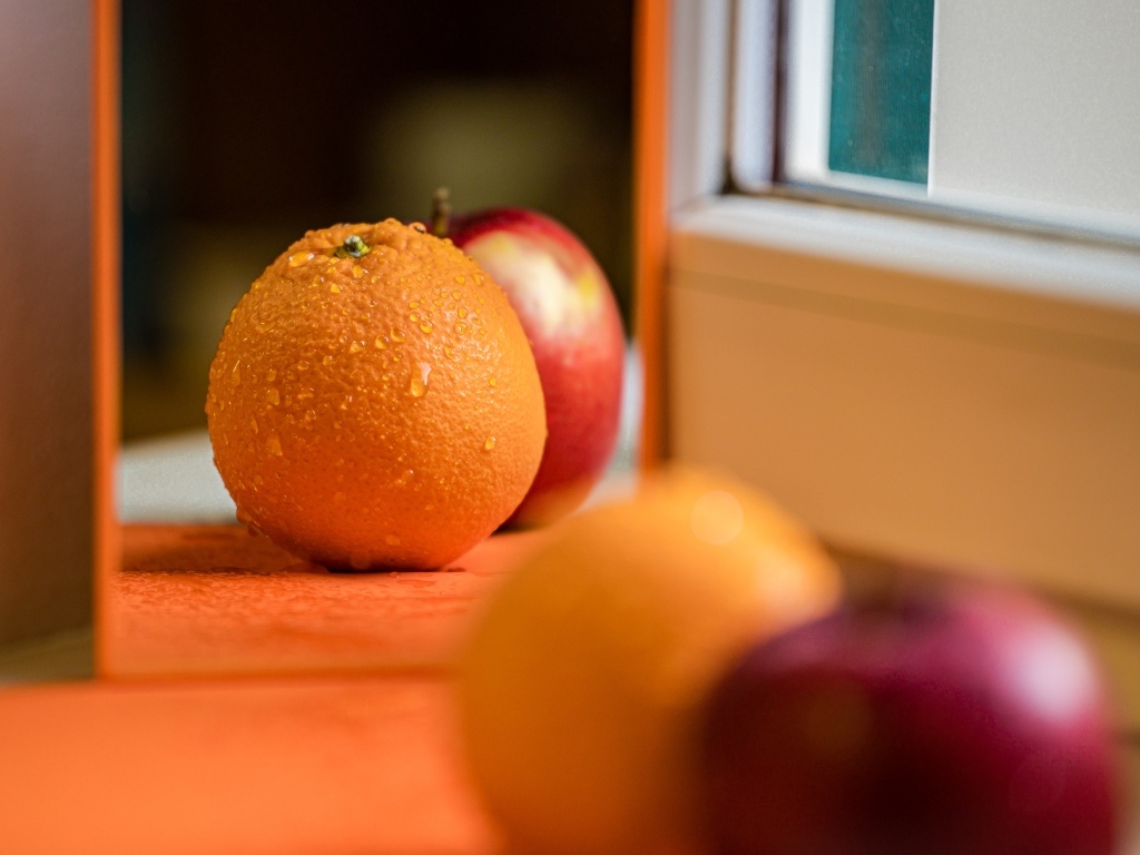 Апельсин и яблоко отражаются в зеркале