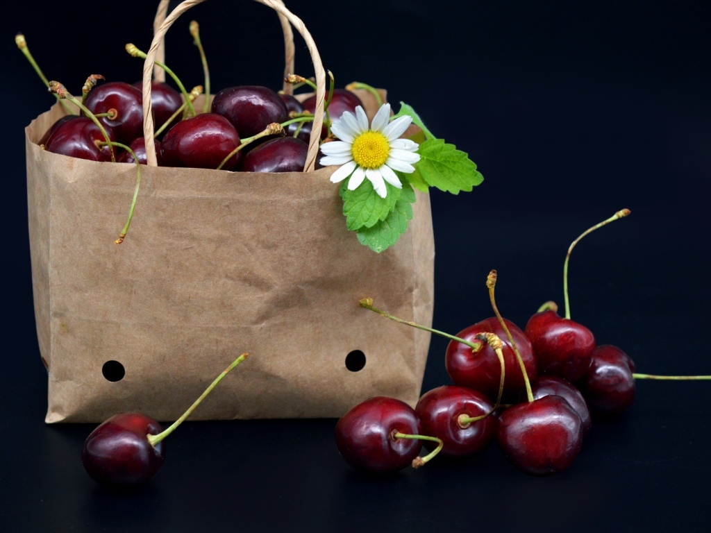 Бумажный пакет с ягодами черешни на черном фоне