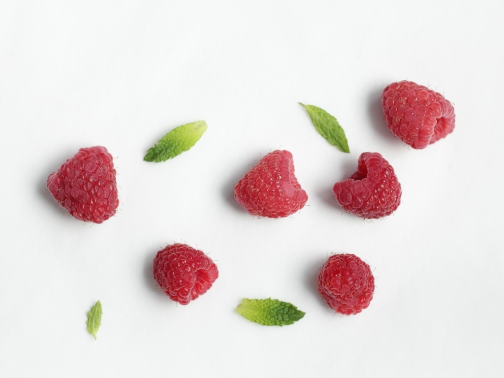 Красная малина с зелеными листьями на белом фоне