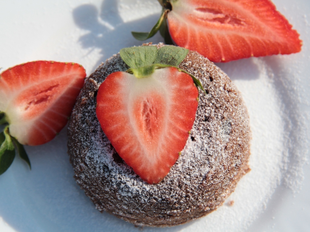 Пирожное на  тарелке с клубникой и сахарной пудрой