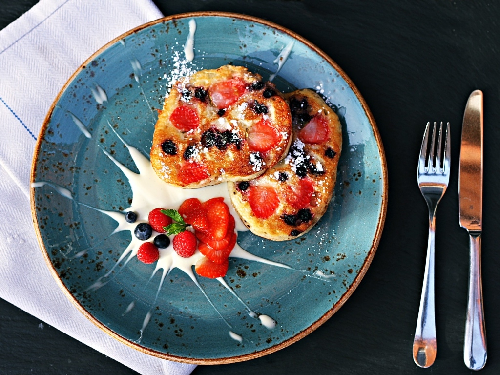 Оладьи на тарелке с ягодами и сметаной