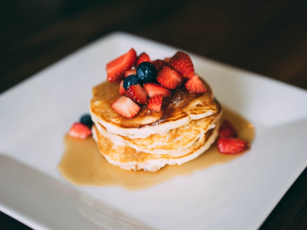 Оладьи с кусочками клубники, медом и черникой на тарелке