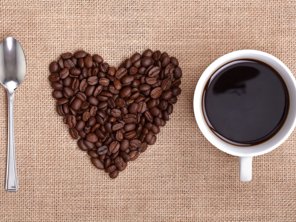 Ложка, сердце из кофейных зерен и белая кружка на столе