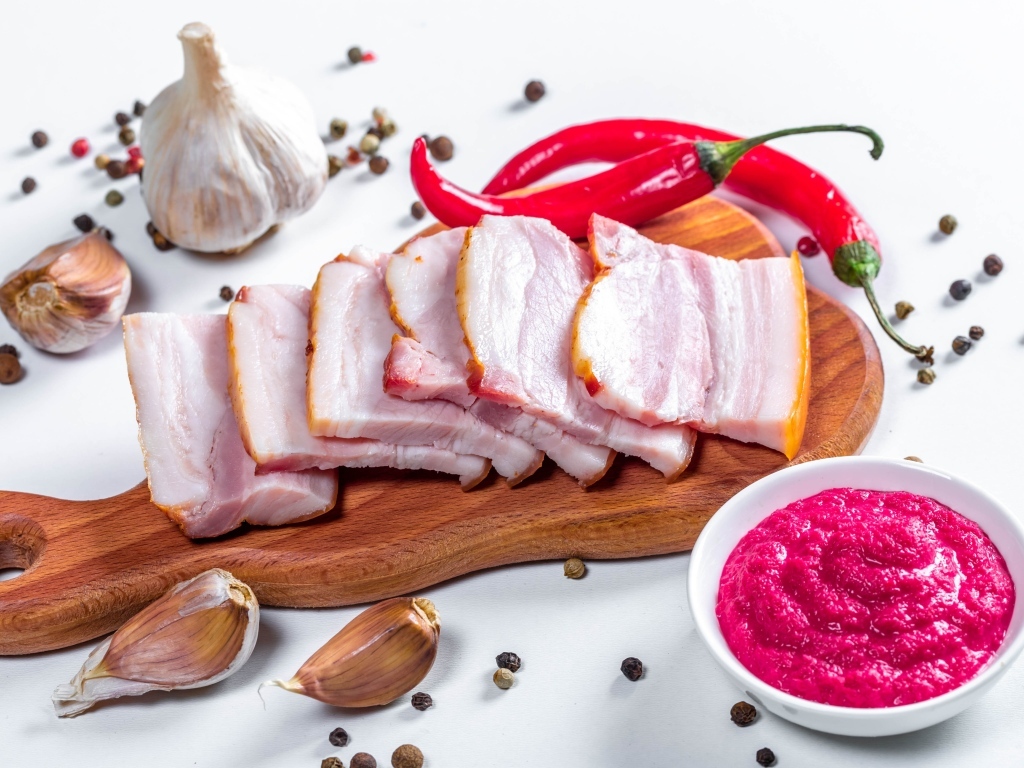 Нарезанное сало на столе с чесноком, хреном и красным перцем