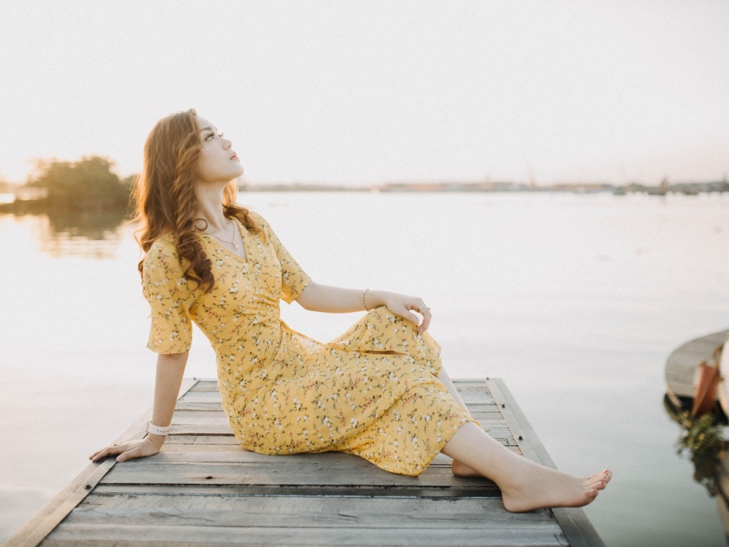 Красивая девушка в платье сидит на мосту у реки