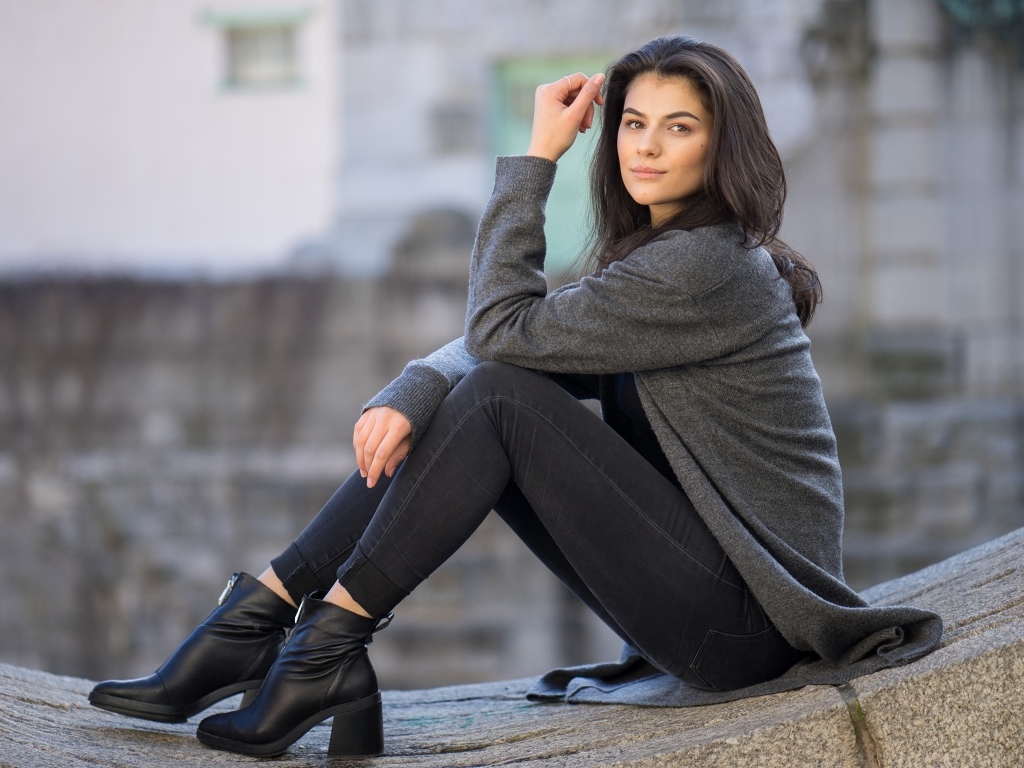 Милая девушка в сером наряде сидит на бетонной плите