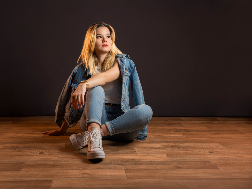 Девушка в джинсовом костюме сидит на полу