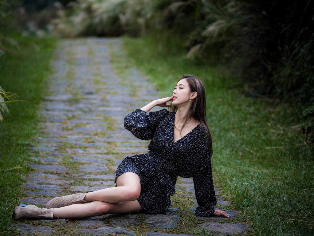 Девушка азиатка в платье лежит на дороге в парке